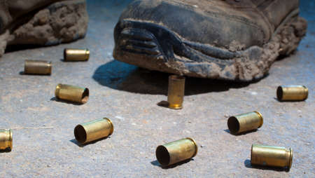 Boots covered in mud and surrounded by handgun brass on concreteの写真素材
