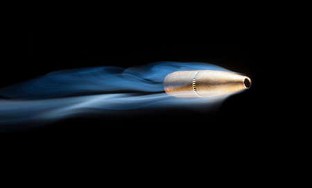 Bullet that has a copper color with smoke behind on a black backgroundの写真素材