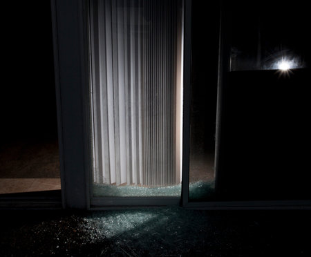 Shattered glass door on a house with a flashlight inside at night