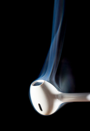One earphone on a black background with smoke rising