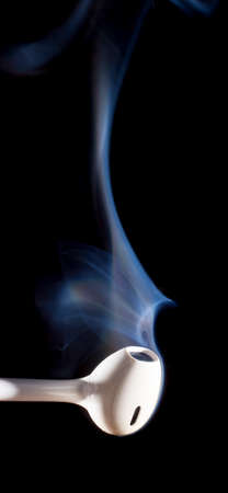 Smoke rising from a pair of white ear buds on a black backgroundの写真素材