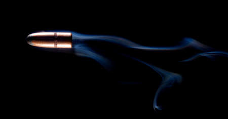Bullet with a copper coating and lead core with smoke behind on blackの写真素材