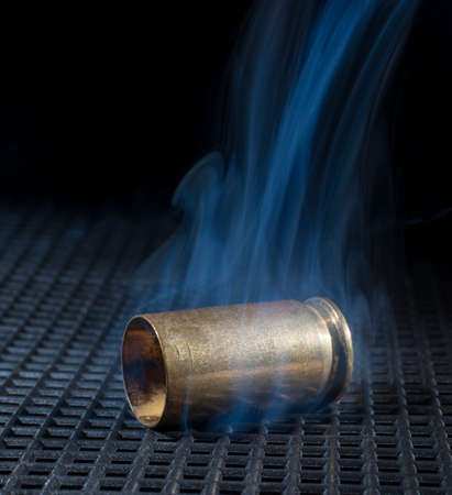 Empty brass from a semi automatic handgun on a black grate with smokeの写真素材