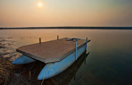 Lake in Canada at sunrise with a pontoon boat on shoreの写真素材
