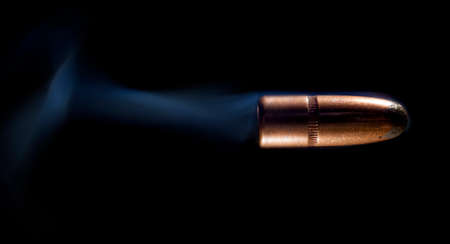 Lead bullet with copper coating on black and smoke behindの写真素材