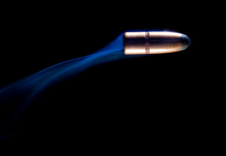 Copper plated bullet on a black background with blue smoke