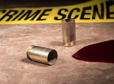Pistol brass and blood on a tan tile with police tape behind