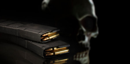 Frightening skull behind a pair of loaded high capacity AR-15 magazines on a black background