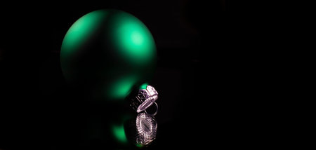 Green Christmas ornament with a black background reflecting on a dark surface.