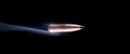 Copper plated bullet on a dark background flying with smoke behindの写真素材