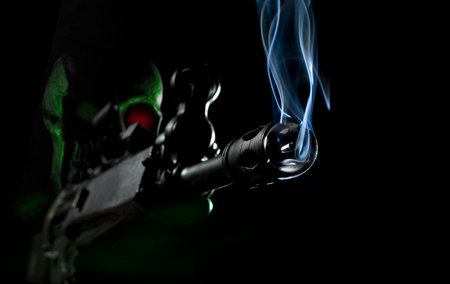 Human skull on an AI robot in the dark with glowing infrared detecting eye holding an assault rifle with smoke coming out on a black background.の写真素材