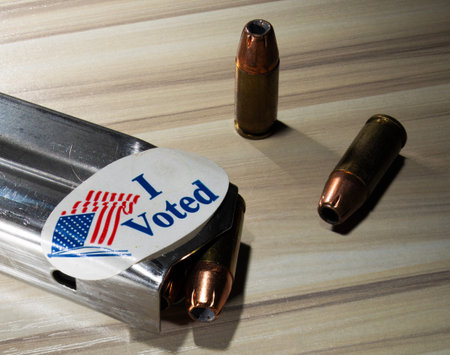 Cartridges next to a stainless steel pistol magazine fully loaded wearing an I voted sticker.