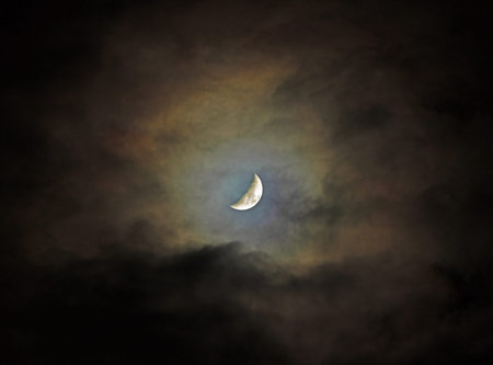Moon shining through a small opening in heavy cloud cover at night.