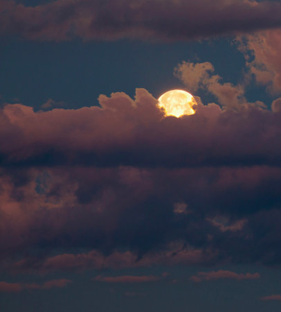 Full moon coming up just after dusk between pink and purple clouds.の写真素材