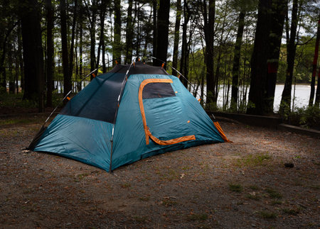 Ideal campsite for a blue backpacking tent in a forest with lake behind that illustrates the attraction of an outdoor lifestyle.の写真素材