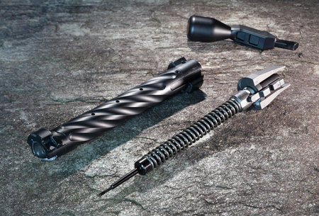 Rifle bolt body, handle, firing pin and spring torn into separate pieces on a bolt-action rifle bolt for maintenance on a rock.の写真素材