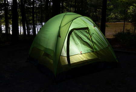 Last fingers of light on the lake seen through the trees with a lighted backpacking tent.の写真素材