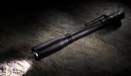 Penlight with a pocket clip and LED on shining brightly on a stone that has shiny muscovite minerals reflecting the light in the dark.の写真素材