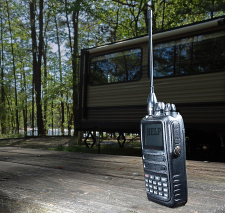 Wooded campsite with a two-way radio displaying the word help with a travel trailer in the forest behind.の写真素材