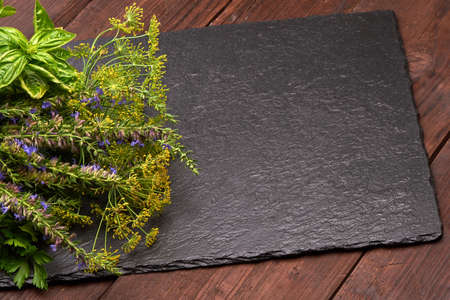 Slate stone plate on a wooden rustic background with green fresh spices. Place for text on a slate stone plateの写真素材