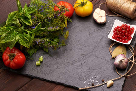 Slate stone plate on a wooden rustic background with fresh spices, colorful tomatoes and red currant. Place for text on a slate stone plateの写真素材