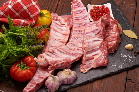Raw pork ribs on a slate stone plate with spices, colorful tomatoes and red currant on a wooden...