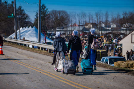 Gordonville, PA, USA - March 10, 2018: Amish women walking with packs and cases to carry what they bought at the annual Lancaster County Mud Sale at the Gordonville Fire Company.のeditorial素材