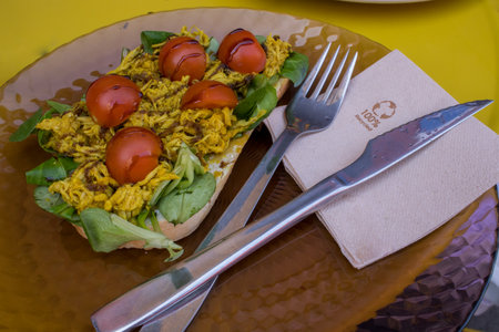 Breakfast in which you can see a toast with chicken, lamb's lettuce, and tomatoes on a yellow table. Breakfast concept.の写真素材