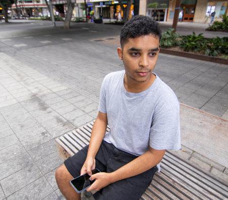 Young boy looking at his cell phone on a benchの写真素材