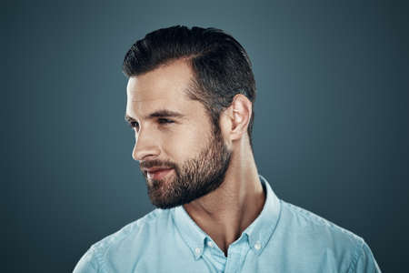 So charming! Handsome young man smiling and looking away while standing against grey backgroundの写真素材