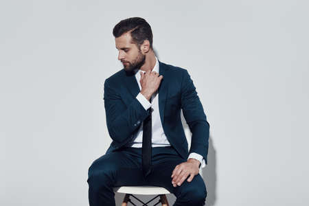 Overworked. Handsome young man pulling his collar while sitting against grey backgroundの写真素材