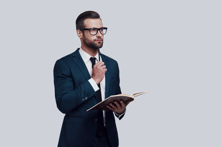 Thinking about solution. Handsome young man writing something down while standing against grey backgroundの写真素材