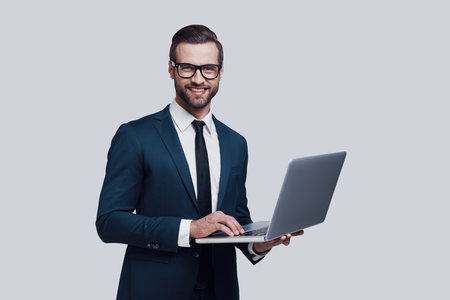 May I help you? Handsome young man looking at camera and smiling while standing against grey backgroundの写真素材