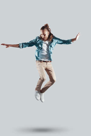 Mid-air fun. Full length of handsome young man keeping arms outstretched while hovering against grey backgroundの写真素材