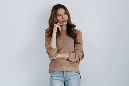 Lost in thoughts. Beautiful young woman looking away while standing against grey backgroundの写真素材