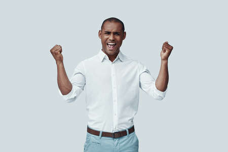 Cheering. Handsome young African man gesturing and smiling while standing against grey backgroundの写真素材