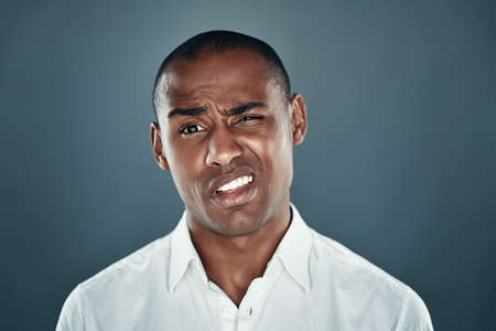 Feeling uncertain. Young African man in shirt looking at camera and frowning while standing against grey backgroundの写真素材