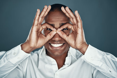 Acting silly. Handsome young African man in shirt making a face while standing against grey...