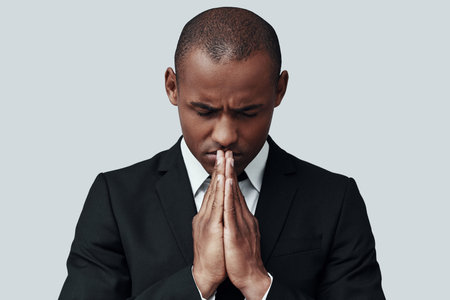 Some decisions are hard. Young African man in formalwear keeping hands clasped while standing...