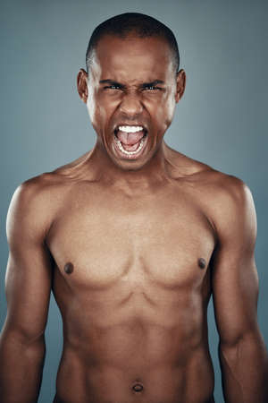 Furious man. Shirtless young African man looking at camera and shouting while standing against grey backgroundの写真素材