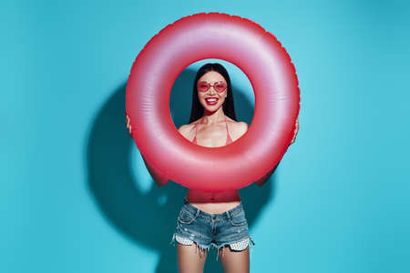 Time to have fun. Attractive young Asian woman smiling and looking at camera while standing against blue backgroundの写真素材