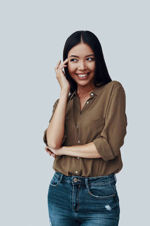 Shy beauty. Attractive young Asian woman looking away and smiling while standing against grey backgroundの写真素材