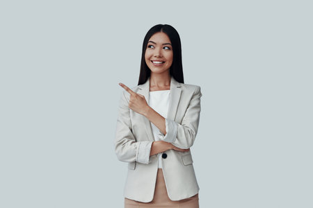 And here comes... Attractive young Asian woman looking away and pointing copy space while standing...