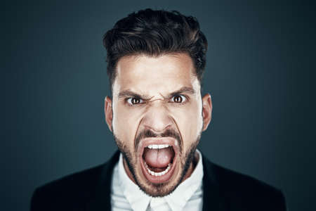 Angry young man making a face and looking at camera while standing against grey backgroundの写真素材