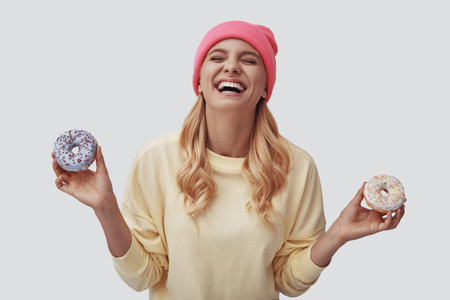 Attractive young woman holding donuts and smiling while standing against grey background