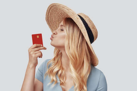 Attractive young woman kissing credit card while standing against grey backgroundの写真素材