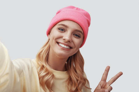 Self portrait of attractive young woman looking at camera and smiling while standing against grey backgroundの写真素材