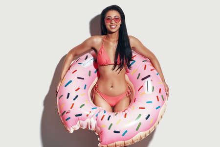 Attractive young woman in bikini looking at camera and smiling while standing against grey backgroundの写真素材