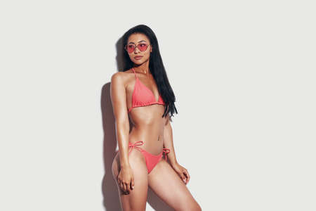 Attractive young woman in bikini looking away while standing against grey backgroundの写真素材