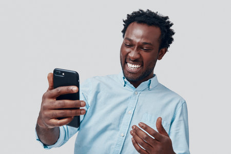 Handsome young African man talking using video conference and smiling while standing against grey...